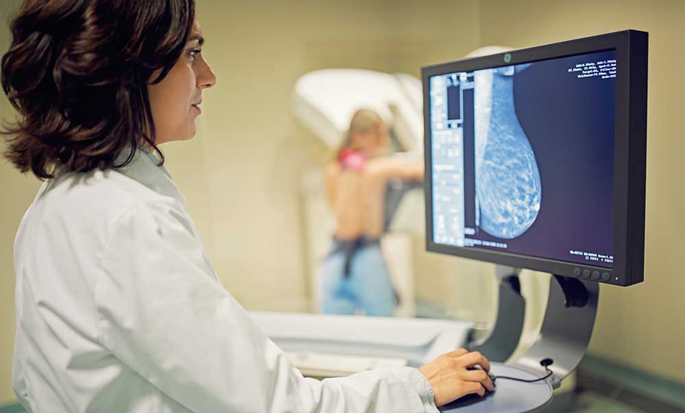 GettyImages-1136026402cropped Woman doctor looking at a breast scan with patient near mammogram machine in the background
